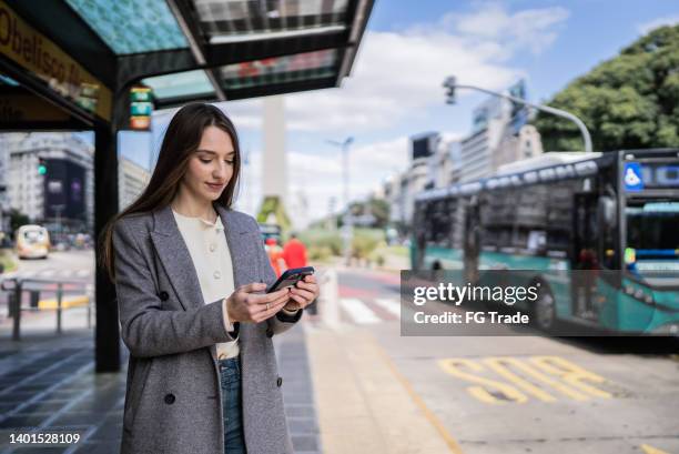 young woman using the mobile phone at the bus stop - uber in buenos aires argentina stock pictures, royalty-free photos & images