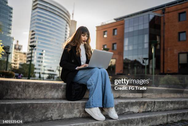 businesswoman sitting outdoors and using laptop - op schoot stockfoto's en -beelden