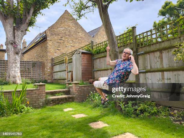 reifer mann, der auf einer seilschaukel schwingt, während er einen arbeitsanruf entgegennimmt - schaukel mann stock-fotos und bilder