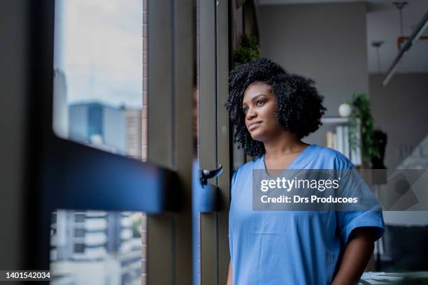 schwarze krankenschwester schaut aus dem fenster - krankenschwester portrait stock-fotos und bilder