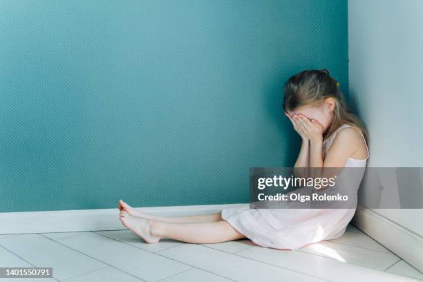 little sad and depressed blond girl in white dress sitting on the floor in the corner indoors. copy space - violence fotografías e imágenes de stock