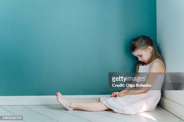 little sad and depressed blond girl in white dress sitting on the floor in the corner indoors. copy space - penalty foto e immagini stock