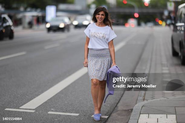 Anna Wolfers seen wearing a white shirt with front floral print, a purple knit sweater, a short skirt with floral print and purple espadrilles on...