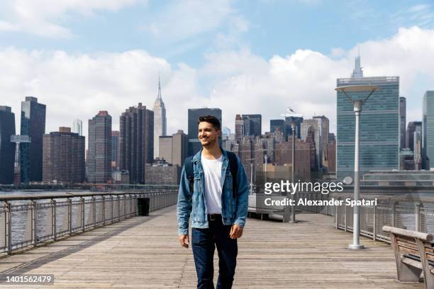 young happy smiling man walking on a pier with manhattan skyline behind him, new york city, usa - city life authentic stockfoto's en -beelden