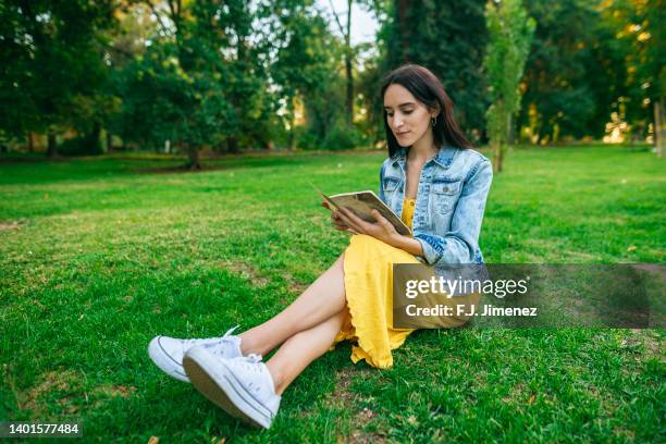 woman reading notebook in the park - denim jacket stock pictures, royalty-free photos & images