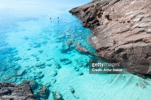 idyllic cian waters in the menorca island with couple doing paddleboard in the mediterranean sea. - private island stock-fotos und bilder