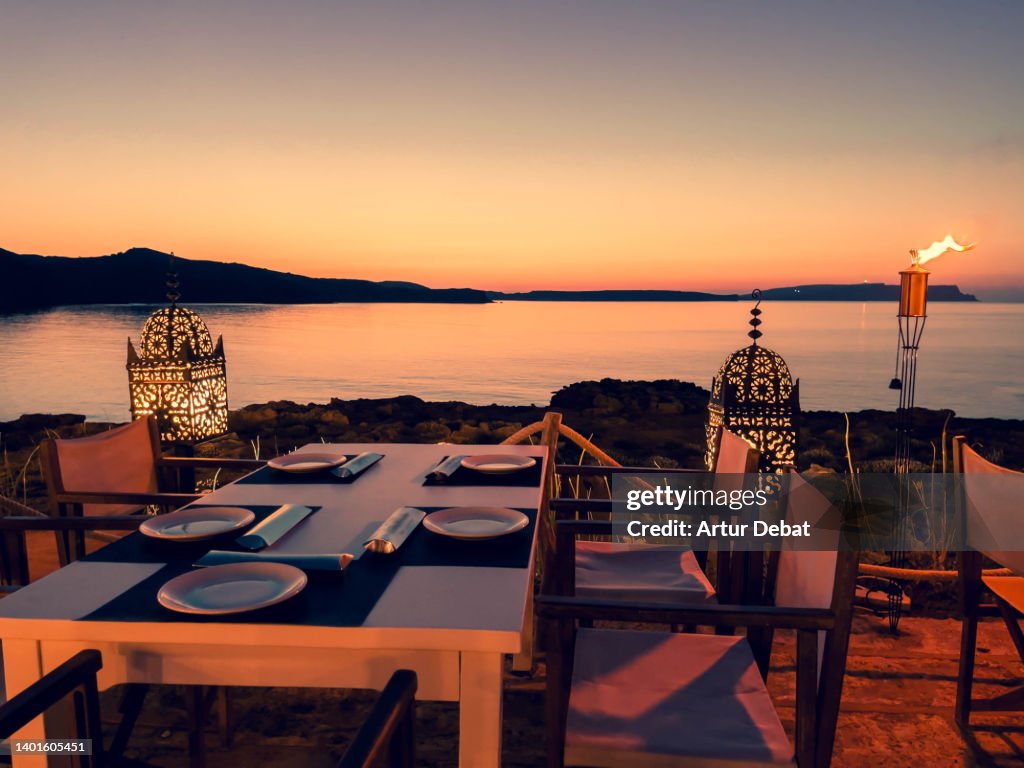 Romantic table for diner next to the sea with beautiful sunset sky.