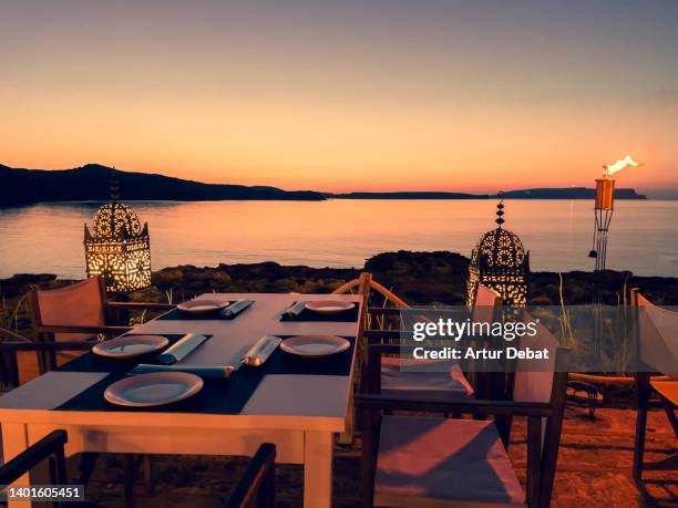 romantic table for diner next to the sea with beautiful sunset sky. - romantiek kunststroming stockfoto's en -beelden