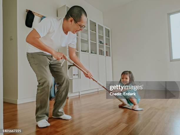 después de limpiar el piso, el padre sostiene a su hija en la fregona - mocha fotografías e imágenes de stock