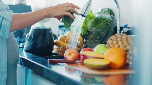 Pregnant diet. Pregnant woman washes fruits and prepares healthy cocktail on the modern kitchen