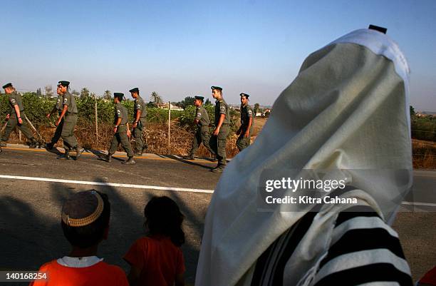 Soldiers walk past a religious Jewish man in the midst of the early morning prayer service near the Israeli village of Kfar Maimon, on July 19, 2005....