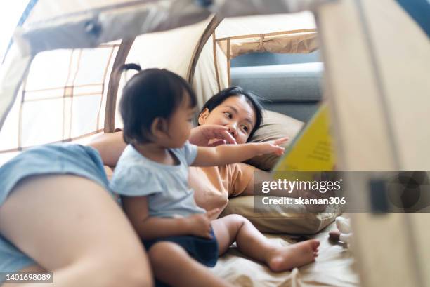 close up facial positive emotion asian mother teaching daughter reading a book inside the camping tent weekend activity. - campfire storytelling stock pictures, royalty-free photos & images