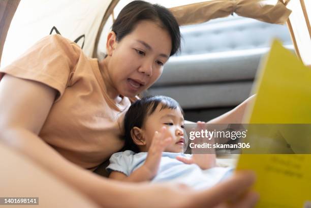 close up facial positive emotion asian mother teaching daughter reading a book inside the camping tent weekend activity. - campfire storytelling stock pictures, royalty-free photos & images