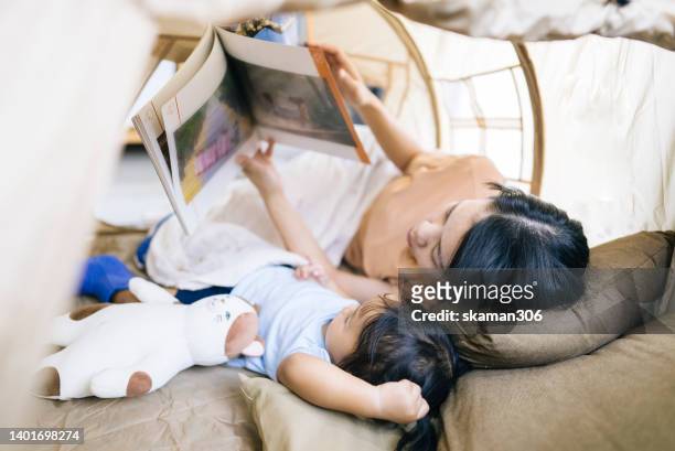 close up facial positive emotion asian mother teaching daughter reading a book inside the camping tent weekend activity. - campfire storytelling stock pictures, royalty-free photos & images