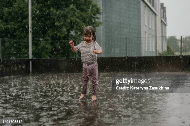 a cute toddler girl fully wet running in the rain - puddle fotografías e imágenes de stock