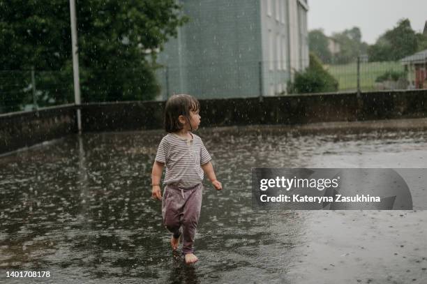 a cute toddler girl fully wet running in the rain - standing in the rain girl stock pictures, royalty-free photos & images