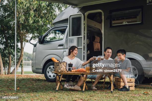 glückliche asiatische familie, die sich am picknicktisch am wohnmobilanhänger in der natur unterhält - happy family asian stock-fotos und bilder