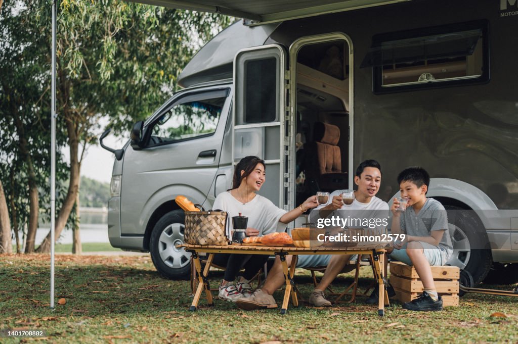 Happy Asian family talking at picnic table by the camper trailer in nature