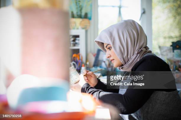 focused young female artist in hijab painting ceramics in art studio - religious service stock-fotos und bilder