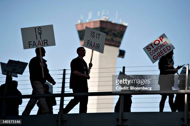 An airport control tower stands in the background as members of Transportation Workers Union Local 521 demonstrate outside American Airlines Terminal...
