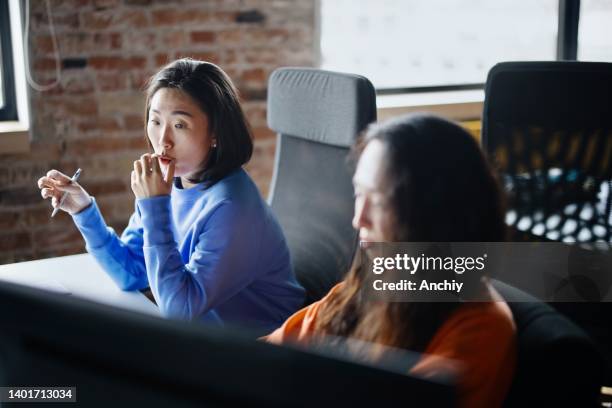female coworkers discussing coding on laptop while sitting in office - hackathon stock pictures, royalty-free photos & images