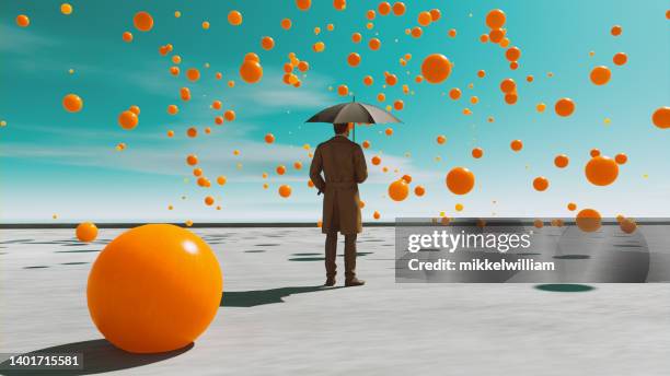 orange balls fall from the sky while man with umbrealla looks at them - blowing up balloon stock pictures, royalty-free photos & images