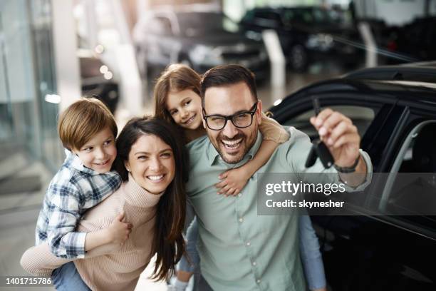 happy family piggybacking after buying a new car in a showroom. - carro novo imagens e fotografias de stock