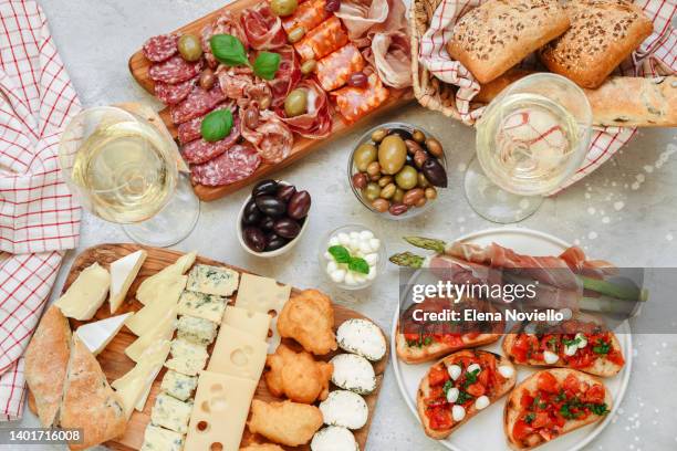 food for lunch and dinner or aperitifs bruschetta with tomatoes and mozzarella, asparagus with bacon.  food antipasto prosciutto ham, salami, olives and bread . cheese on a board parmesan, pecorino, gorgonzola. two glasses of white wine or prosecco - menu on table stock pictures, royalty-free photos & images