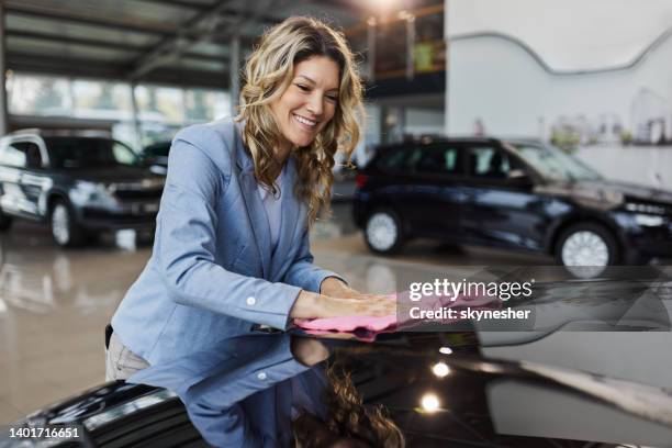 happy car salesperson polishing the car in a showroom. - clean car stock pictures, royalty-free photos & images