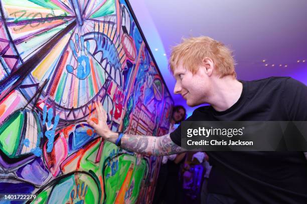 Ed Sheeran puts his hand print on a painting by by Sacha Jafri during the Ruth Strauss Foundation's #RockforRuth event at The Wormsley Estate on June...