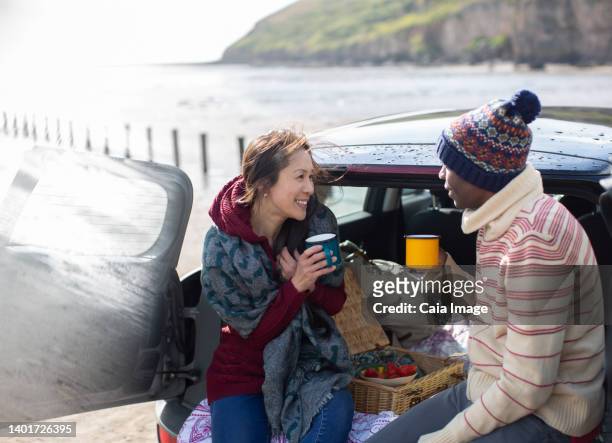happy couple drinking coffee at back of car on beach - mature couple winter outdoors stockfoto's en -beelden
