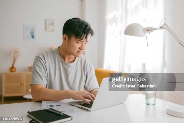 young asian boy working from living room at home. - asian man home laptop stock pictures, royalty-free photos & images