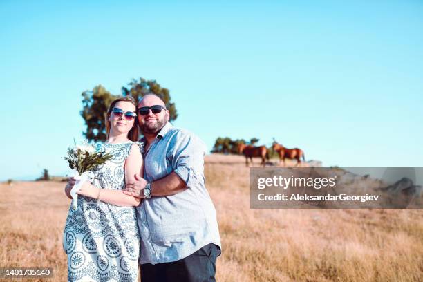 romantisches paar, das spaß am hang hat und sich mit pferden im rücken umarmt - wedding feet stock-fotos und bilder