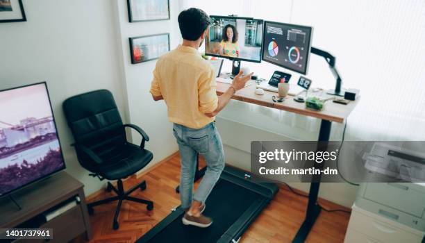 man at standing desk home office talking on business video call - treadmill test stockfoto's en -beelden