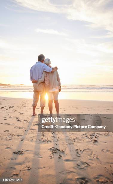 loving senior couple watching a sunset on a sandy beach - idyllic retirement stock pictures, royalty-free photos & images
