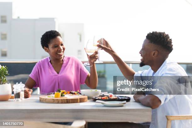 coppia alza bicchieri celebrando la bella vita godendosi il pranzo insieme in un bar sul tetto - rooftop dining foto e immagini stock