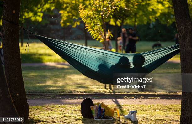 young couple relaxing in hammock at green city area - romantic picnic stockfoto's en -beelden