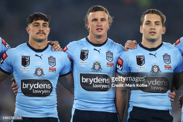 Kotoni Staggs, Jack Wighton and Cameron Murray of the Blues stand for the national anthem before game one of the 2022 State of Origin series between...
