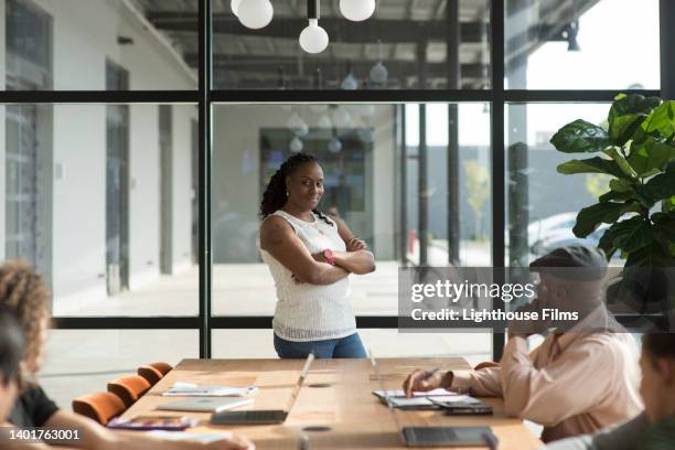 portrait of businesswoman standing at head of conference table - sonrisa satisfecha fotografías e imágenes de stock