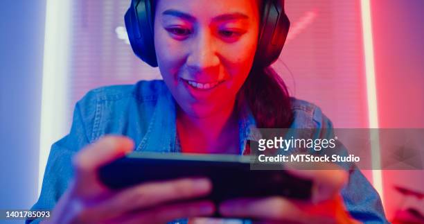 close up of young asian woman playing online smartphone video game and broadcast streaming live in neon lights living room at home. - game experience stock pictures, royalty-free photos & images