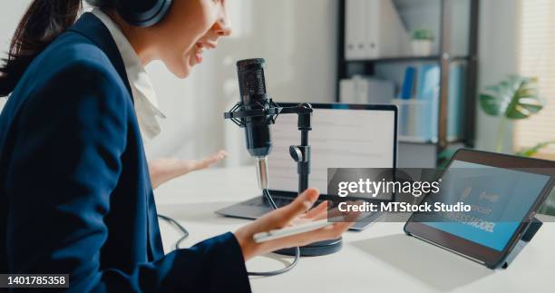 close up of young asian businesswoman recording and broadcasting a podcast on her laptop from studio office. - asian journalist stock pictures, royalty-free photos & images