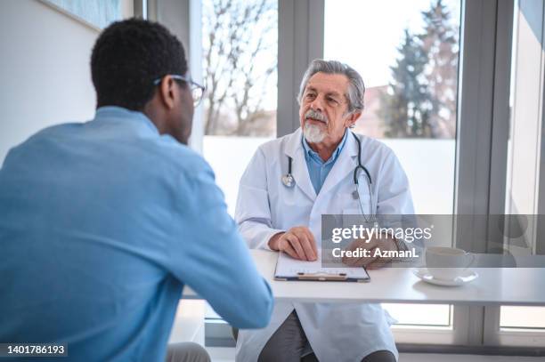 young african american male patient checking his test results with a senior caucasian ophthalmologist - uroloog stockfoto's en -beelden