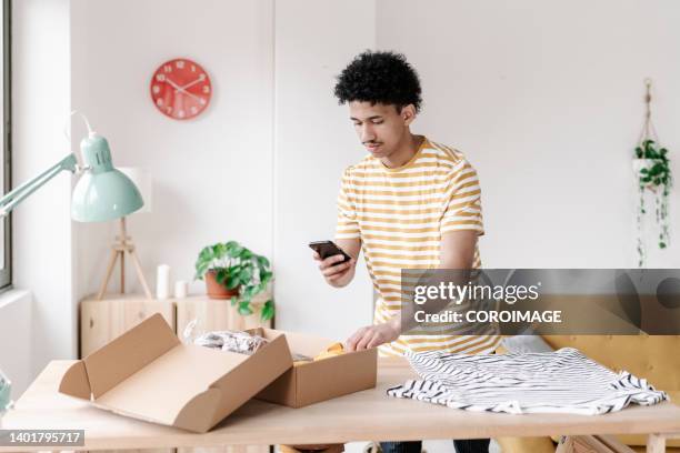 young man in office taking a photo of one to a box full of clothes he has sold. - photographing clothes stock pictures, royalty-free photos & images