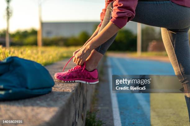 donna atleta irriconoscibile che lega le scarpe su un campo sportivo - calzature sportive foto e immagini stock