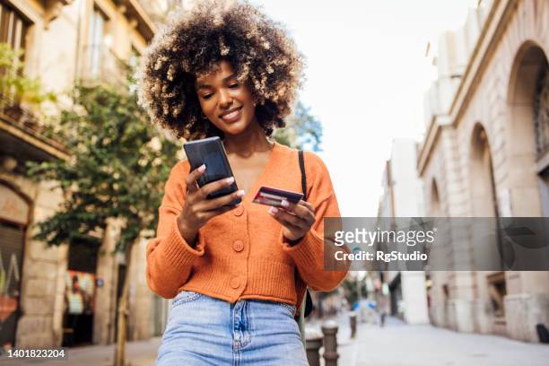glückliches afro-mädchen in barcelona, das unterwegs online einkauft - credit card stock-fotos und bilder
