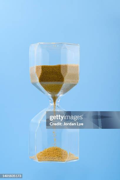 gold color sand hourglass on blue colored background. - time is money stock pictures, royalty-free photos & images