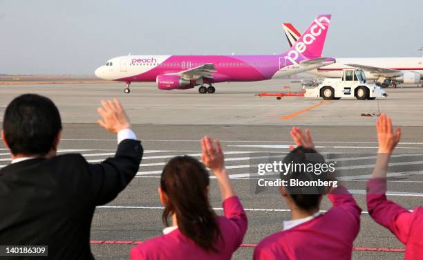Ground staff members wave as a Peach Aviation Ltd. Airbus SAS A320 airplane taxis for take off at Kansai International Airport in Izumisano City,...