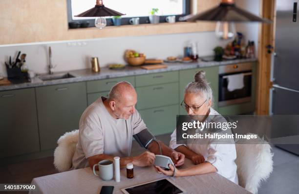 high angle view of seniors couple sitting in kitchen, measuring blood pressure and taking pills. - high blood pressure stockfoto's en -beelden