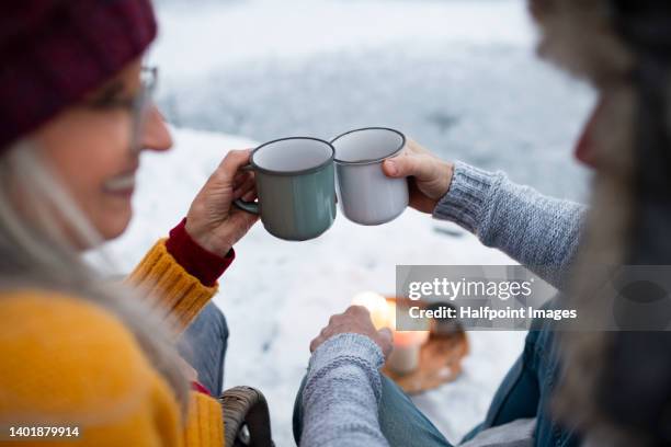 close-up of seniors hand holding cups of tea in winter, outdoor scene with snow. - hygge stockfoto's en -beelden