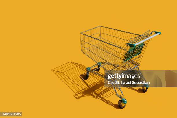 view of an empty shopping cart on an isolated yellow background. - grocery cart fotografías e imágenes de stock